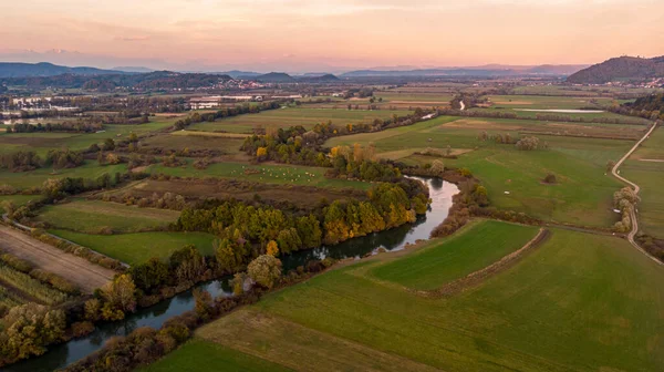 Panorama aéreo espetacular do rio que flui através de campos ao pôr do sol. — Fotografia de Stock