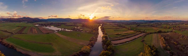 Spectacular aerial panorama of river flowing through fields at sunset. Royalty Free Stock Photos