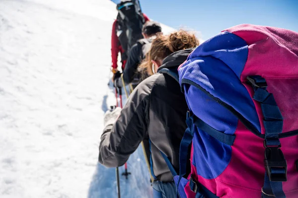 Rope team member point of view with mountaineers walking on snow and ice in sunny weather.