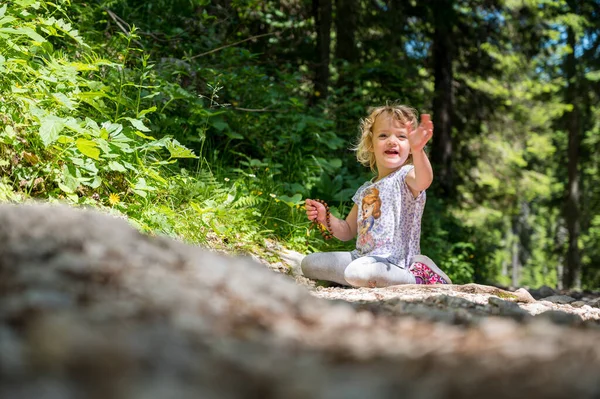 Menina loira bonito sentado em uma trilha florestal apreciando a natureza. — Fotografia de Stock