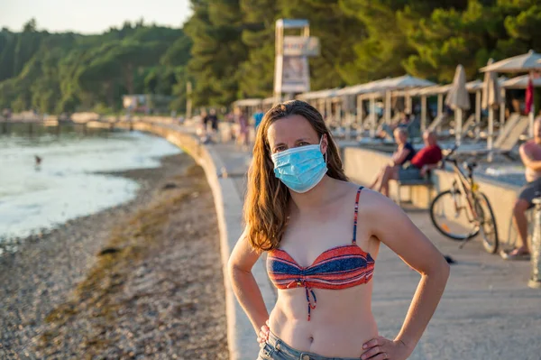 Młoda kobieta w masce medycznej na plaży podczas zachodu słońca. — Zdjęcie stockowe