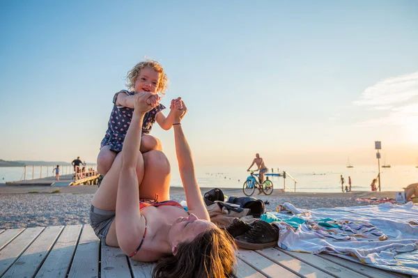 Young mother wearing medical mask playing with her daughter at the beach. New normal concept.
