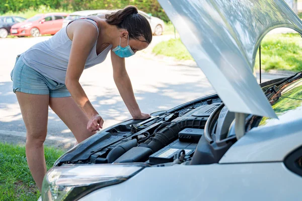 Woman wearing medical mask trying to fix broken car engine. — Stock Photo, Image