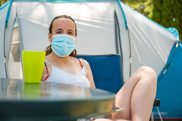 리조트에서 캠핑 텐트 앞에 앉아 의료용 마스크를 쓴 여자. 로열티 프리 스톡 이미지