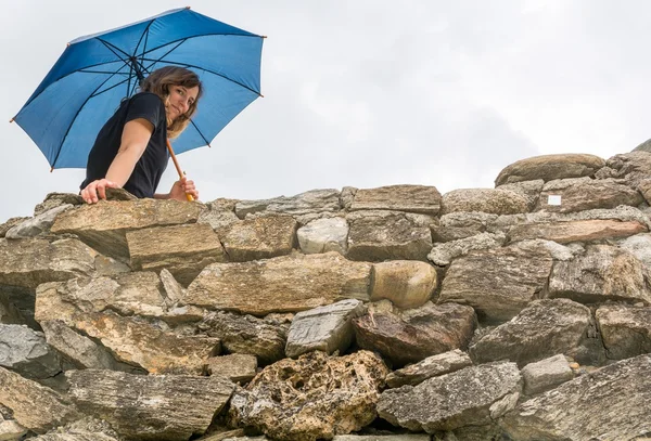 Menina segurando um guarda-chuva olhando para baixo de uma parede — Fotografia de Stock