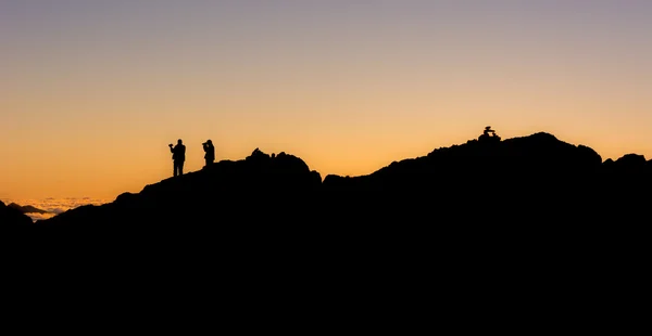 Silueta de personas de pie en una cresta de montaña — Foto de Stock