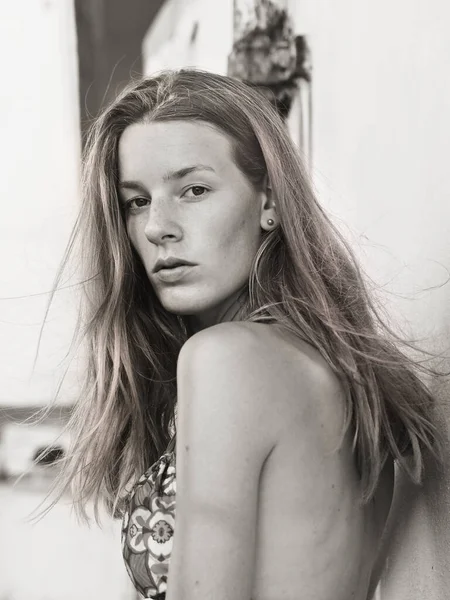 Half body side portrait of a young woman with long hair and bikini top in black and white. Half-open lips, astonished facial expression. The model is without make-up and very natural.