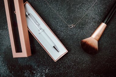 Makyaj fırçası, beyaz kalem ve gümüş gerdanlık.