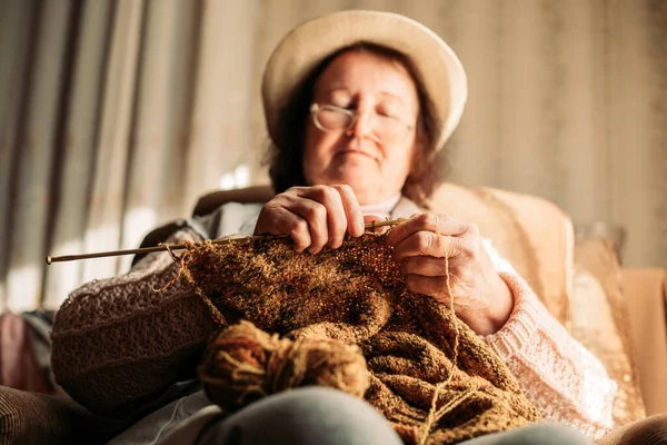 Elderly woman knitting sweater for her grandchildren. Focus on the needles