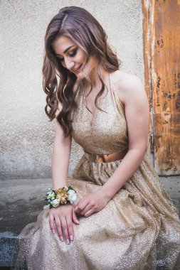 Göz kamaştırıcı altın elbiseli güzel bir genç kız elinde aksesuarlarla oturuyor.