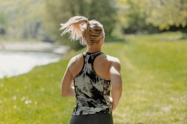 Spor giysili genç sarışın kızın arka plan fotoğrafı. Sabahları nehir kenarında koşuyor. Güneşli bir kazak. Sağlıklı yaşam tarzı ve spor anlayışı