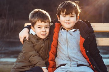 İki tatlı erkek kardeş, bir bankta oturup birbirlerine sevgi gösteriyorlar..