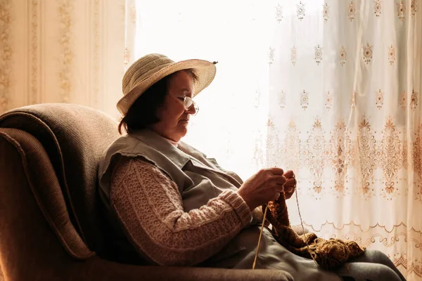 Starsza Kobieta Szydełkująca Sweter Dla Wnuków Przy Oknie — Zdjęcie stockowe