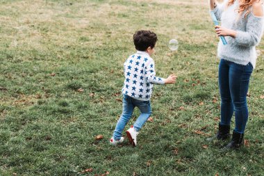 Sabun köpüğü yapan annesinin etrafında koşan küçük çocuk.