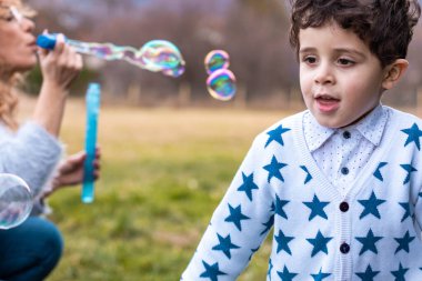Annesi oğluyla dışarıda oynuyor. Baloncuklu sabun köpüğü yapmak