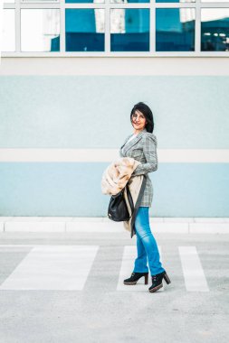 Kürk ceketli ve kot pantolonlu modern orta yaşlı kadın.