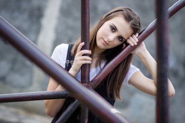 Dışarıdaki esmer bir kızın portresi, metal çitlere yaslanmış.