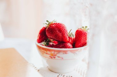 Masadaki seramik haykırışta taze çilekler ve bir kitap. Sabah keyfi zamanı.