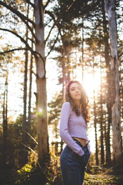 Genç, esmer kız ormanda yürüyor.