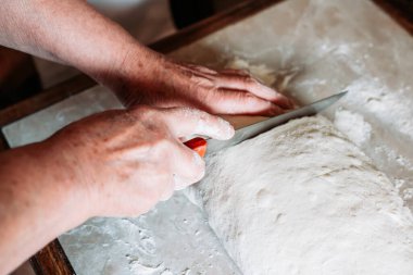 Kadın elleri masada çiğ ekmek hamuru parçaları kesiyor. Ev yapımı yemek.