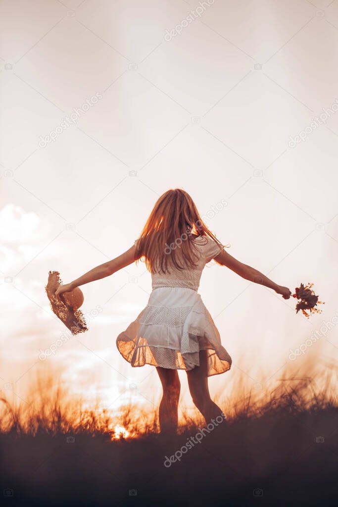 Outdoors photo of young, teen, ginger girl running through the field, holding a summer hat. Copy space