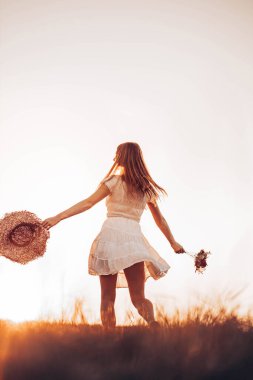 Elinde yaz şapkasıyla tarlada koşan genç, kızıl bir kızın açık havada çekilmiş fotoğrafı. Boşluğu kopyala