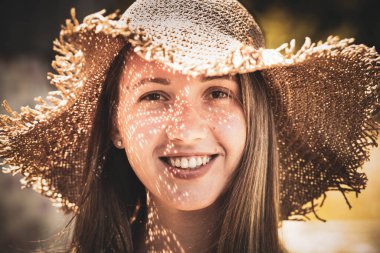 Yazlık şapkalı, gülümseyen genç bir kadın.