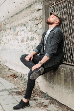 Duvara yaslanmış sarmaşık şapkalı yakışıklı bir adamın portresi.