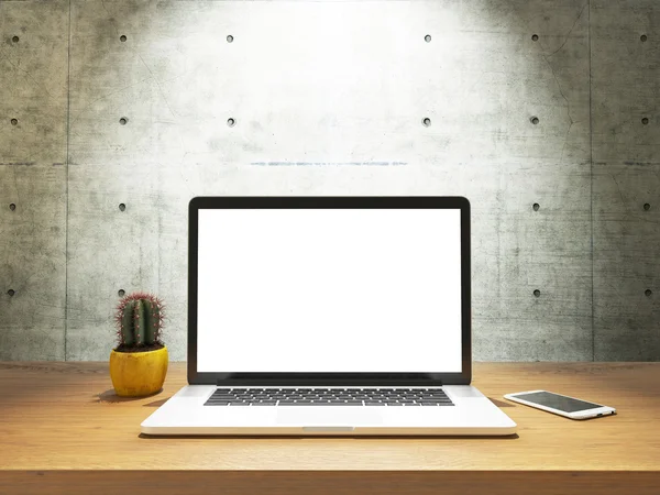 Laptop e telefone com tela em branco na parede de concreto frontal da mesa — Fotografia de Stock