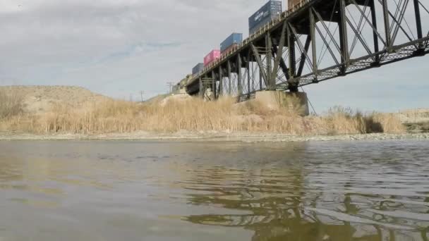 Stort tåg passerar en metallbro med bäck i förgrunden. Rio Grande, El Paso, Texas. — Stockvideo