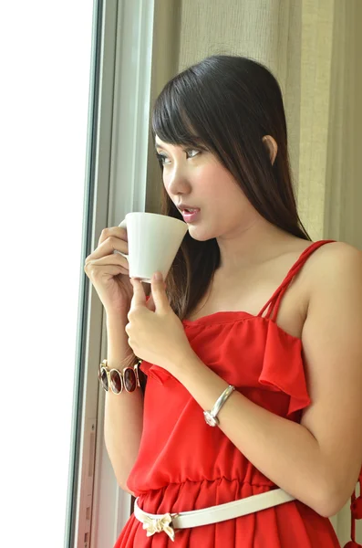 Beautiful girl with cup of coffee looking out of window — Stock Photo, Image