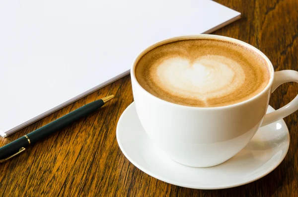 Ένα φλιτζάνι καφέ με σχήμα καρδιάς, στυλό και ανοιχτό κενό βιβλίο — Φωτογραφία Αρχείου