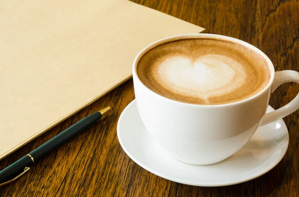 Ένα φλιτζάνι καφέ με σχήμα καρδιάς, στυλό και κενό βιβλίο — Φωτογραφία Αρχείου