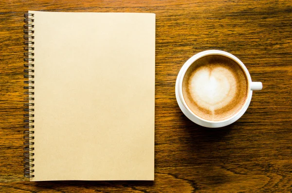 A cup of coffee with heart shape and open blank book on wood bac — Stock Photo, Image