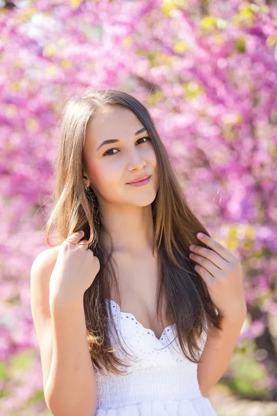 Молодая красивая девушка в белом сарафане стоит рядом с деревом с цветами, цвецкие деревья, розовые цветы, весна, солнце, счастье, нежность, сирень — стоковое фото