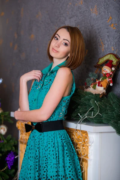 Beautiful young girl sitting on the floor on a background of green trees, she is dressed in a green dress. She smiles, she has red hair, big eyes, she stands by the fireplace — Stockfoto