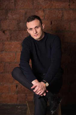 wealthy man, dark background, short-haired man, businessma, a man in a dark  sweater, blazer, looking directly into the camera, stern look, business, brick wall, dark background, red brick, bright smile,