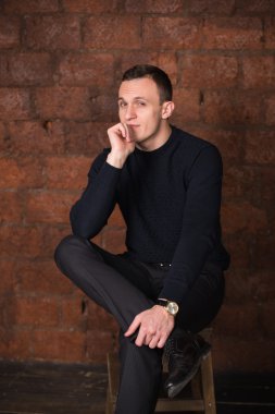 wealthy man, dark background, short-haired man, businessma, a man in a dark  sweater, blazer, looking directly into the camera, stern look, business, brick wall, dark background, red brick, bright smile,