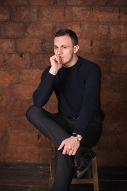 wealthy man, dark background, short-haired man, businessma, a man in a dark  sweater, blazer, looking directly into the camera, stern look, business, brick wall, dark background, red brick, bright smile,