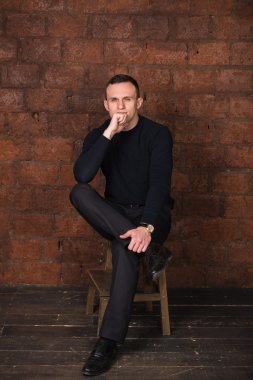 wealthy man, dark background, short-haired man, businessma, a man in a dark  sweater, blazer, looking directly into the camera, stern look, business, brick wall, dark background, red brick, bright smile,