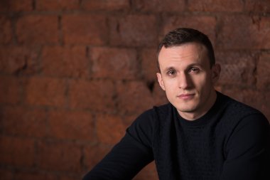 wealthy man, dark background, short-haired man, businessma, a man in a dark  sweater, blazer, looking directly into the camera, stern look, business, brick wall, dark background, red brick, bright smile,