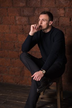 wealthy man, dark background, short-haired man, businessma, a man in a dark  sweater, blazer, looking directly into the camera, stern look, business, brick wall, dark background, red brick, bright smile,