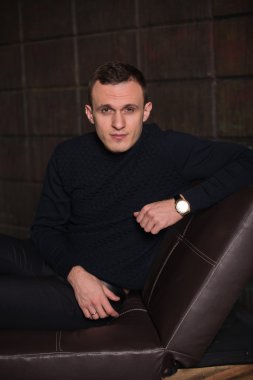 wealthy man, dark background, short-haired man, businessma, a man in a dark  sweater, blazer, looking directly into the camera, stern look, business, brick wall, dark background, red brick, bright smile,