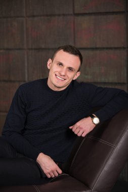 wealthy man, dark background, short-haired man, businessma, a man in a dark  sweater, blazer, looking directly into the camera, stern look, business, brick wall, dark background, red brick, bright smile,