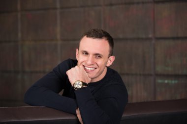 wealthy man, dark background, short-haired man, businessma, a man in a dark  sweater, blazer, looking directly into the camera, stern look, business, brick wall, dark background, red brick, bright smile,
