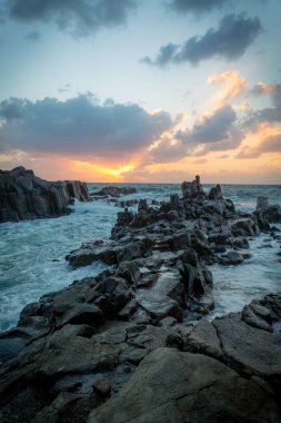 Arka planda günbatımı ve vahşi bir deniz olan güzel bir kaya oluşumu.