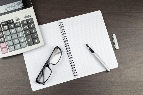 Bloc-notes vide sur la table de bureau avec stylo, calculatrice et lunettes. Vue d'en haut — Photo