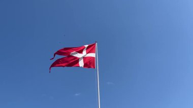 Danimarka ulusal bayrağı, Dannebrog, parlak mavi gökyüzüne gururla el sallıyor, beyaz İskandinav haçı rüzgarda dalgalanırken güneşli bir günde İskandinav amblemi, yatay görüntüler