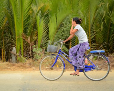 Burmese woman rides bicycle along countryside street