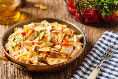 Carbonara soslu tavuk ve biberli makarna, eski bir bakır tavada servis edilir. Ön görünüm.